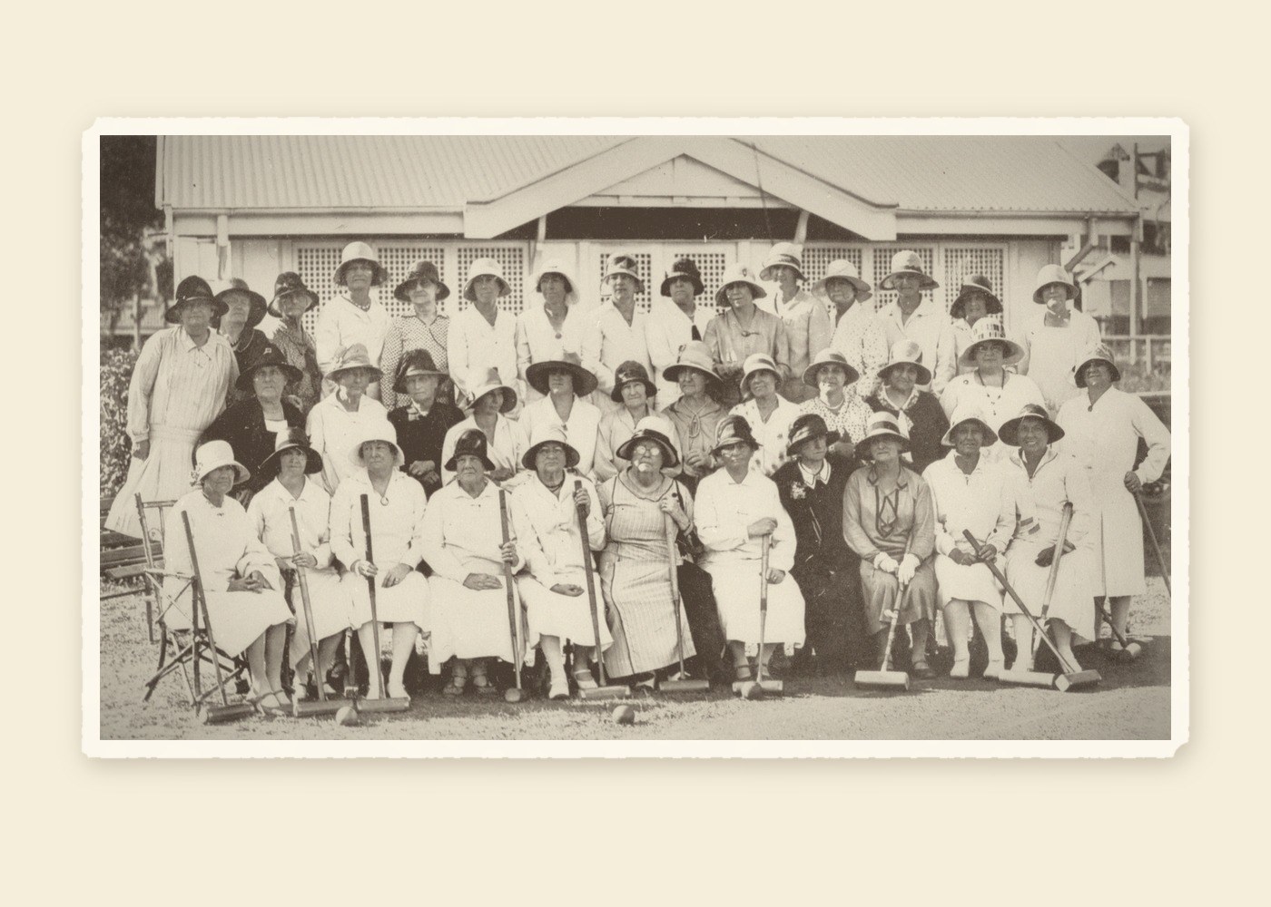 Archival photograph of about forty women of the McIlwraith Croquet Club, Brisbane, in the 1930s, in white dresses and hats with their mallets in front of the clubhouse
